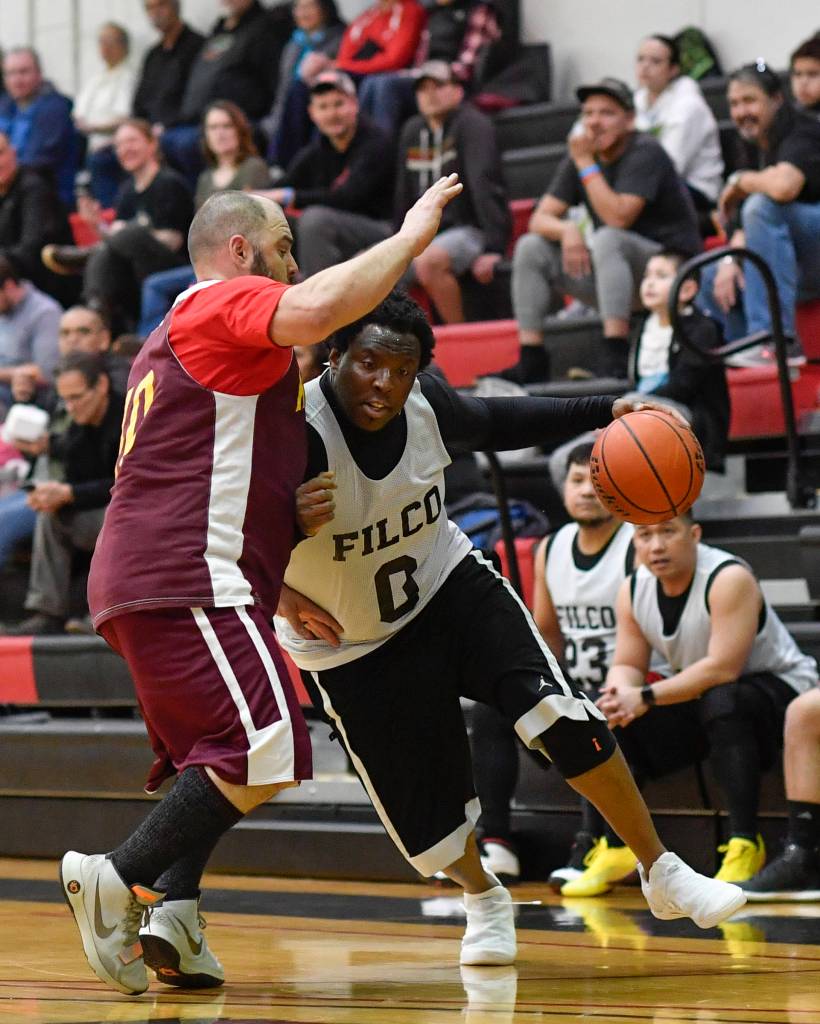 Filcoms Rob Ridgeway, right, drives against Klukwans Stuart DeWitt in their C bracket game at the Gold Medal Basketball Tournament on Thursday, March 21, 2019. (Michael Penn | Juneau Empire)