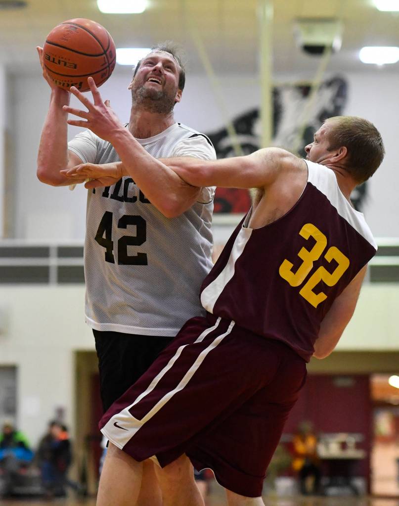 Filcoms Greg Lockwood, left, is fouled by Klukwans Coleman Stanford in their C bracket game at the Gold Medal Basketball Tournament on Thursday, March 21, 2019. (Michael Penn | Juneau Empire)