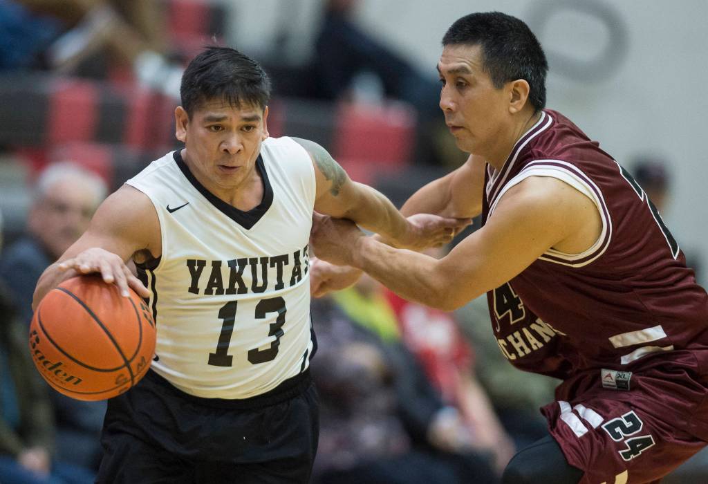 Yakutats Jerry Riddington, left, dribbles away from Hoonahs Ken Willard Jr. in the Masters bracket game at the Gold Medal Basketball Tournament on Thursday, March 21, 2019. (Michael Penn | Juneau Empire)