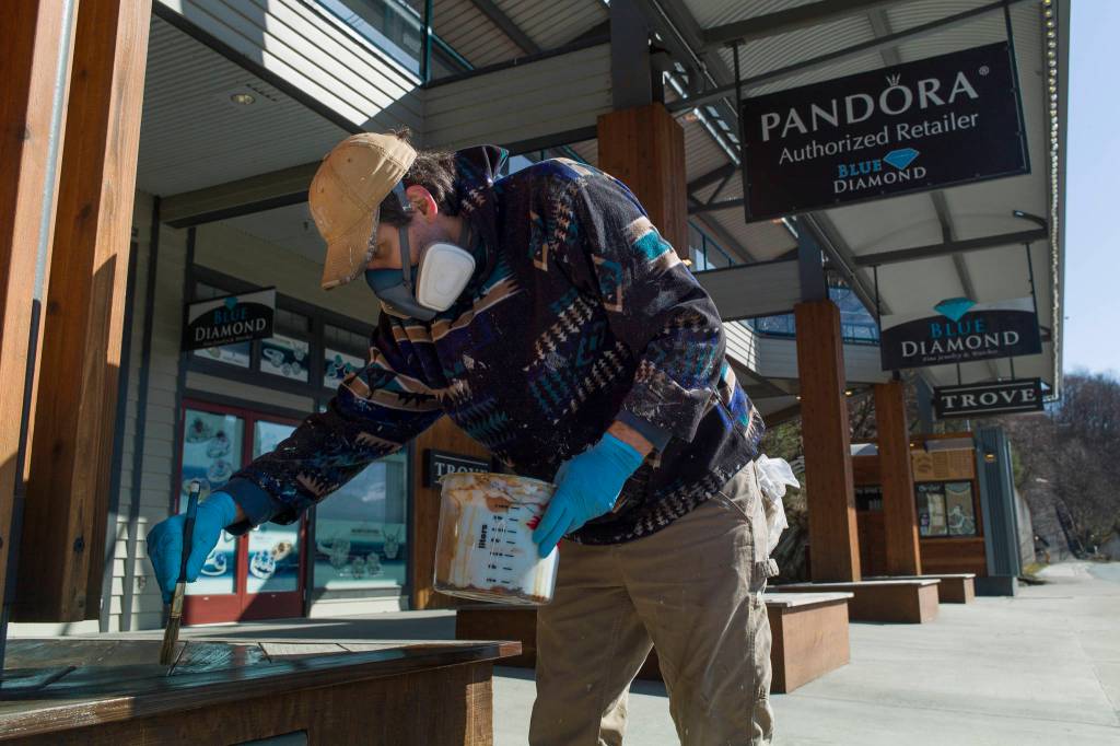 Richard Hotch, of Herrs Painting, gives benches a sealing coat at the Alaska T-Shirt Mall on Friday, March 29, 2019. (Michael Penn | Juneau Empire)