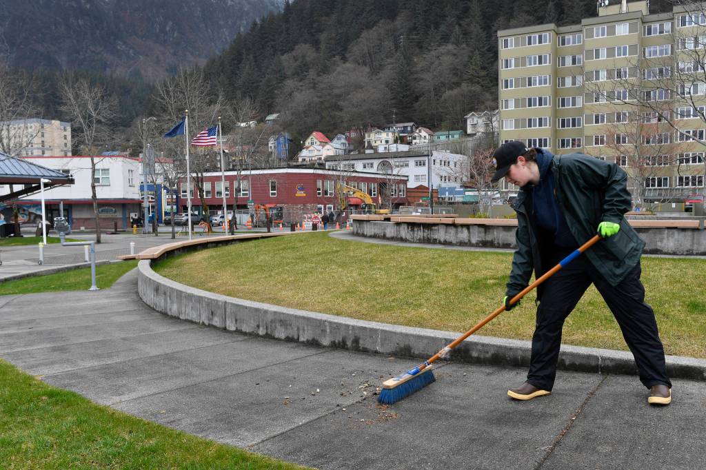 Sarah Mikesell, of the citys Dock and Harbors department, sweeps the sidewalk at Marine Park on Friday, April 19, 2019. (Michael Penn | Juneau Empire)