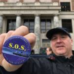 Drew Transkei, of Ketchikan, holds up a pin before a SOS Rally at the Capitol on Tuesday, May 7, 2019. (Michael Penn | Juneau Empire)