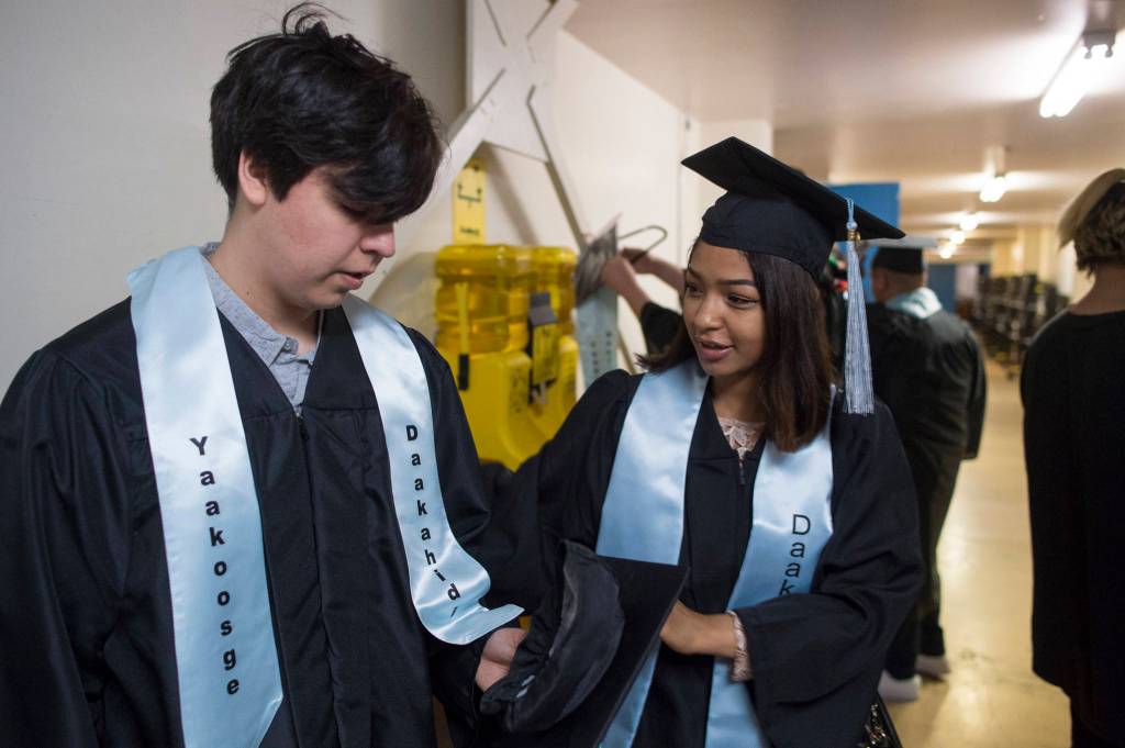Desitny Cleveland-Fey, right, helps Kenneth Brown get ready for the Yaakoosgé Daakahidi High School graduation at Centennial Hall on Sunday, May 26, 2019. (Michael Penn | Juneau Empire)