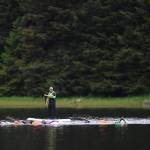 Kevin Sellers follows along on a standup paddle board as swimmers train in Auke Lake on Wednesday, June 5, 2019. (Michael Penn | Juneau Empire)