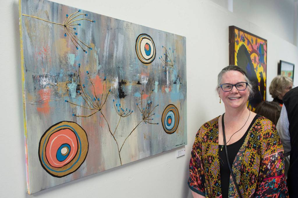 Cameron Vance stands next to her acrylic painting Habitation in the Juneau Arts and Humanities Councils Juried Art Show for First Friday on Friday, June 7, 2019. (Michael Penn | Juneau Empire)