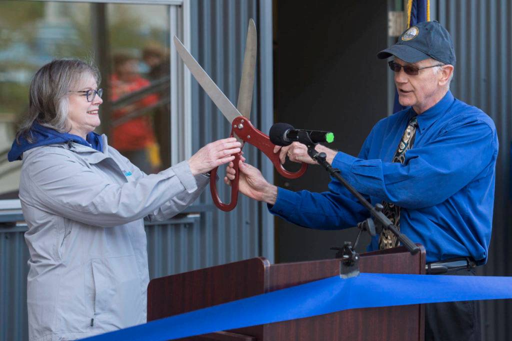 Port Director Carl Uchytil hands oversized scissors toTravel Juneau President & CEO Liz Perry during a ceremony to open the new Visitors Center Kiosk, Friday, May 17, 2019. Uchytil is talking to the Greater Juneau Chamber of Commerce today. (Michael Penn | Juneau Empire)