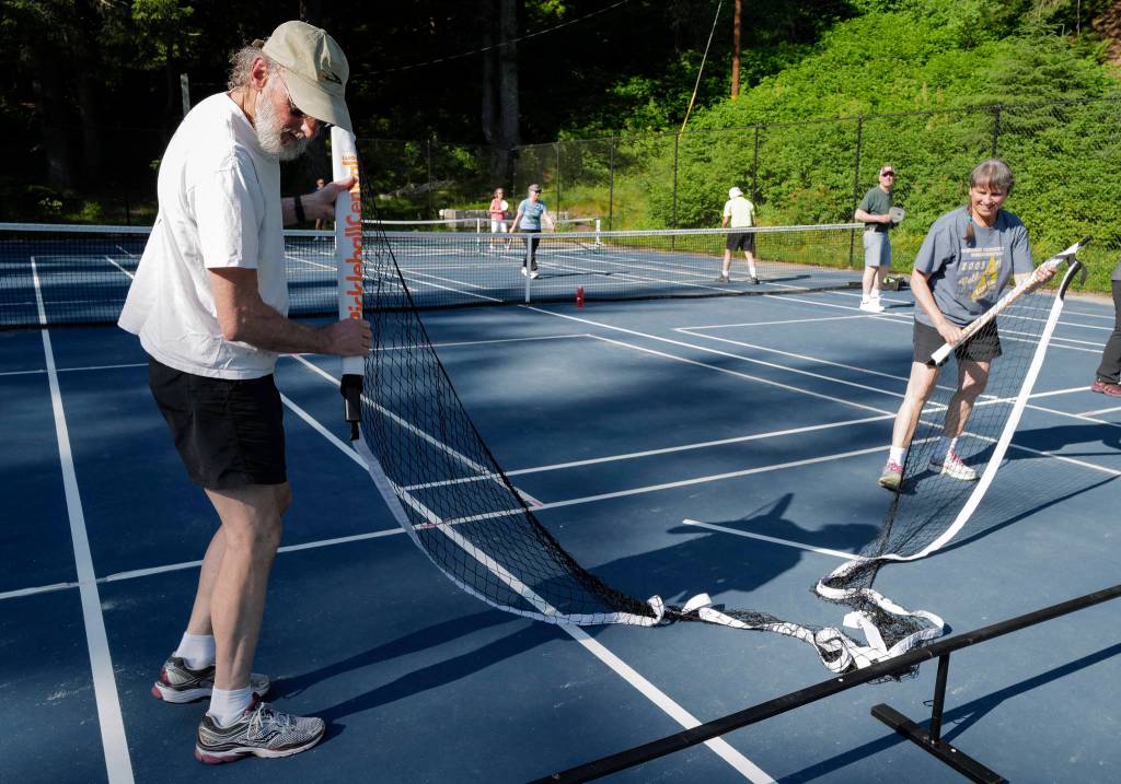 Chas Dense, left, and Christi Herrea set up a portable pickleball net at the Cope Park tennis courts on Wednesday, June 26, 2019. (Michael Penn | Juneau Empire)