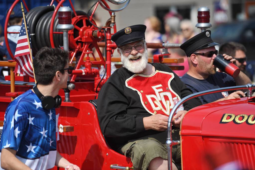 Mike Race, center, rides in Capital City Fire/Rescues 1937 Ford fire engine during the Fourth of July parade on Thursday, July 4, 2019. (Michael Penn | Juneau Empire)