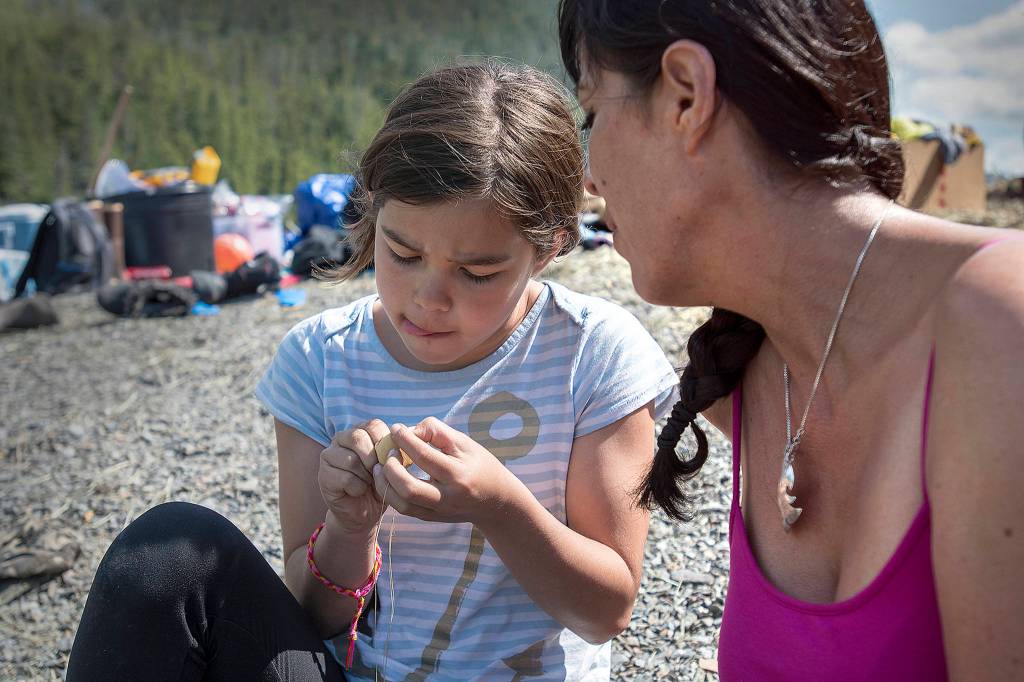 In this photo taken June 20, 2019, Kim Wilson of Ketchikan teaches Shannon McCarty, 12, how to thread and assemble a pair of healing-hand earrings during Culture Camp on Hemlock Island near Metlakatla, Alaska. This year was the first time the Ketchikan Indian Community and Nüüm Na Waalt culture camps joined together for the event and a seven-night campout on the island. (Dustin Safranek/Ketchikan Daily News via AP)