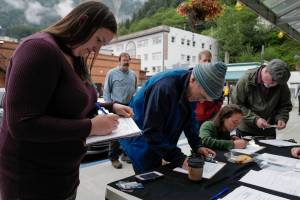 Monika Kunat, left, signs an application petition to recall Gov. Mike Dunleavy with others at the Planet Alaska Gallery on Thursday, Aug. 1, 2019. (Michael Penn | Juneau Empire)