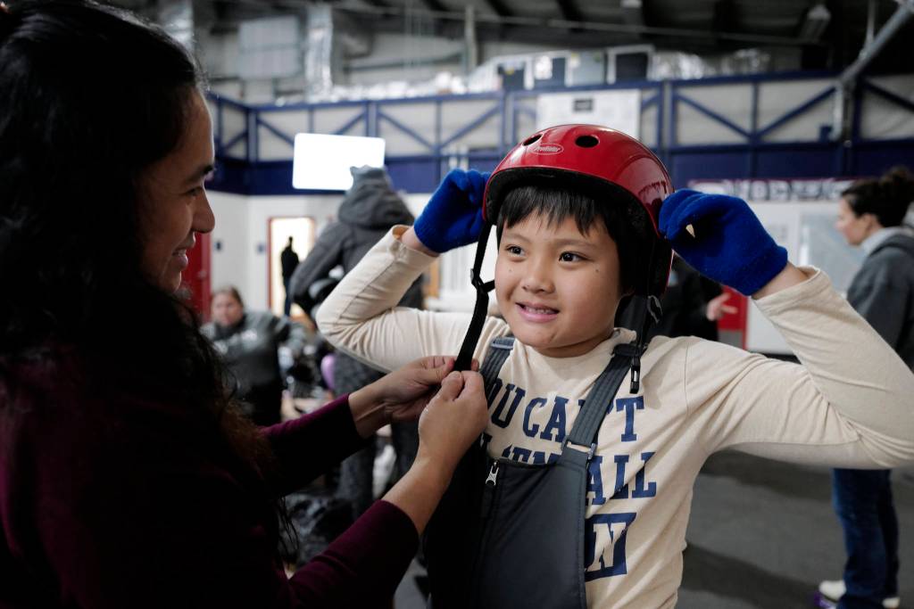 Hazel Yadao adjusts a helmet for her son, Arnold, 9, during a free skate on the opening day at the Treadwell Arena on Monday, Aug. 5, 2019. (Michael Penn | Juneau Empire)