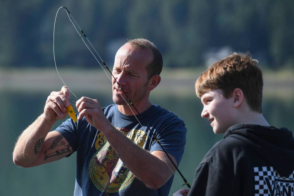Dzantiki Heeni Middle School eighth-grader Riley Kellar, right, is helped by Teacher Bobby Jones while fishing for salmon at the Wayside Park on Channel Drive on Friday, Aug. 30, 2019. The fish will be used in a dog treat business the students are developing to raise money for a water filtering system to be used at the school. Two math teachers, Jones and Tennie Bentz, are having the students start four businesses as a way of teaching the use of math in the real world. (Michael Penn | Juneau Empire)