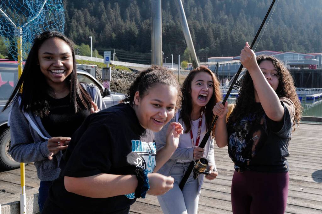 Dzantaki Heeni Middle School eighth-graders Remi Starks, left, Zariah Knight, Dawn Hoit and Charlize Brown, right, react to a salmon on their line at the Wayside Park on Channel Drive on Friday, Aug. 30, 2019. The fish will be used in a dog treat business the students are developing to raise money for a water filtering system to be used at the school. Two math teachers, Jones and Tennie Bentz, are having the students start four businesses as a way of teaching the use of math in the real world. (Michael Penn | Juneau Empire)