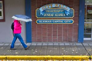 In this October 2015 file photo, maple leaves fall on Seward Street as a pedestrian ducks rain in front of City Hall. (Michael Penn | Juneau Empire File)