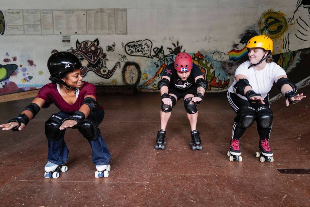 Jennifer Gross, left, and Shabadrang Khalsa, who skate with the Juneau Rollergirls, teach Empire reporter Michael S. Lockett how to rollerskate at the Pipeline Skate Park on Friday, Oct. 11, 2019. (Michael Penn | Juneau Empire)