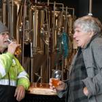 Dave Iverson and Bill Ashby enjoy beers and conversation in front of brewery equipment at Forbidden Peak Brewerys grand opening, Saturday, Oct. 12, 2019. (Ben Hohenstatt | Juneau Empire)