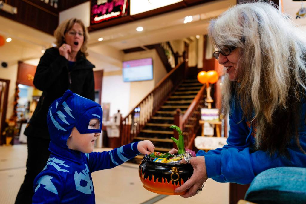 Dorain Gross, left, reacts as her grandson, Thorin Lombard, 3, reaches for a candy dish offered by Michelle of The Bears Lair during the Trick or Treat Downtown event on Thursday, Oct. 31, 2019. More than 70 business put out orange balloons to participate in the event aimed at young children. (Michael Penn | Juneau Empire)