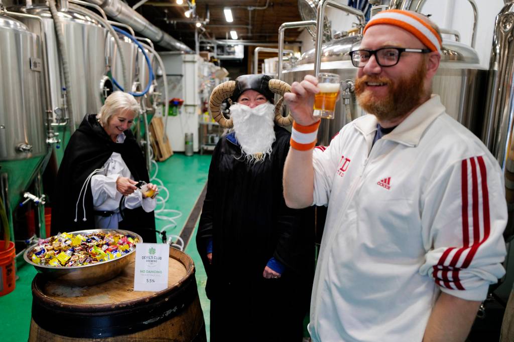 Aaron Suring takes advantage of the adult treat offered by Rachel Sanders, center, and TJ Thomson at the Devils Club Brewing Company during the Trick or Treat Downtown event on Thursday, Oct. 31, 2019. More than 70 business put out orange balloons to participate in the event aimed at young children. (Michael Penn | Juneau Empire)
