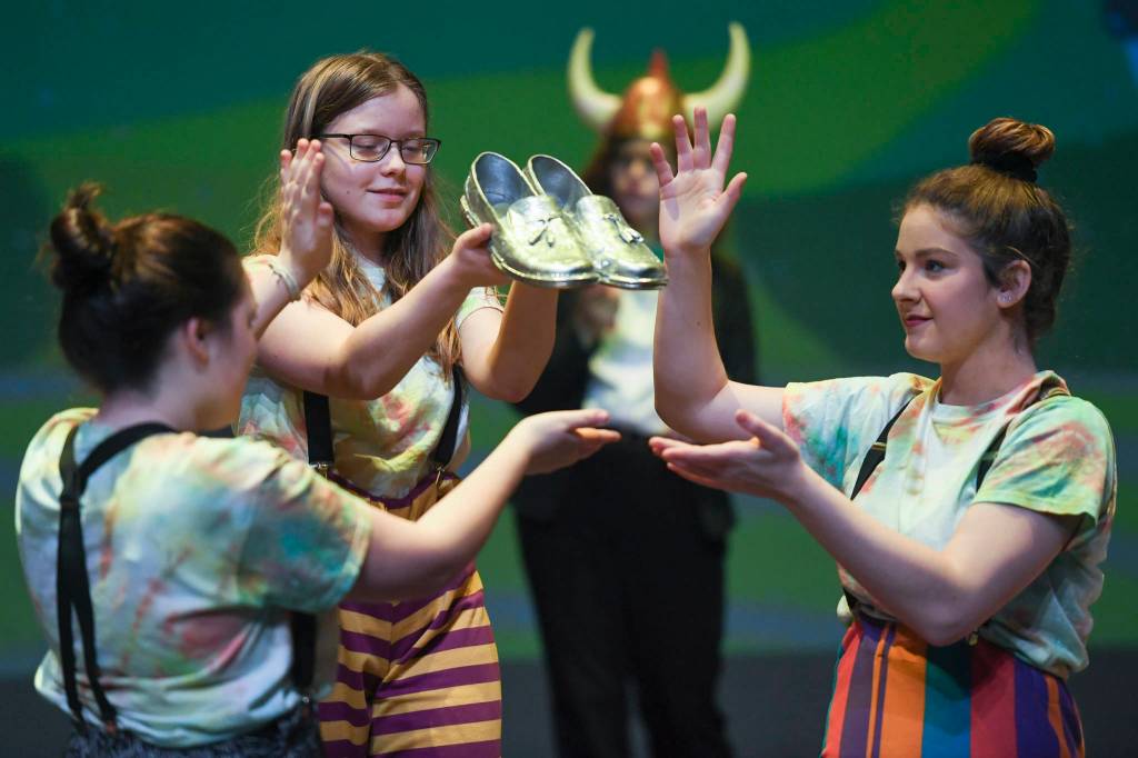 Munchkins Elena Lohrey, Caitlin Parker and River Carroll display the dead witchs shoes during rehearsal for the Thunder Mountain High School production of Choose Your Own Oz at TMHS on Friday, Nov. 8, 2019. (Michael Penn | Juneau Empire)