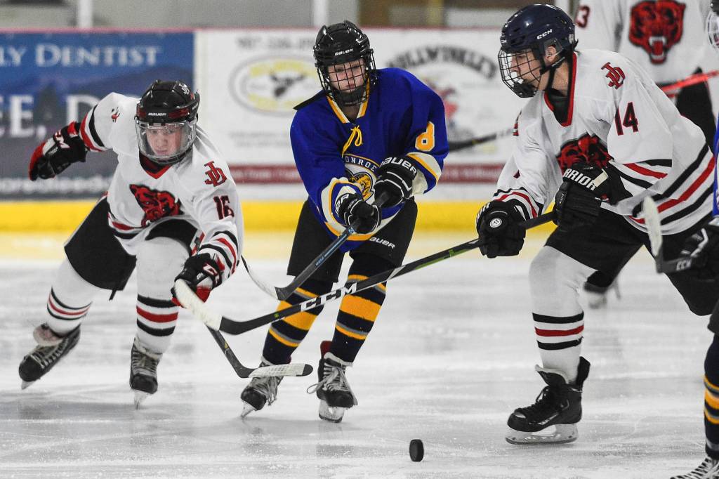 Juneau-Douglas Zac Stagg, left, and Max McHenry, right, take the puck away from Monroe Catholics Bella Knavel at the Treadwell Arena on Friday, Nov. 15, 2019. JDHS won 13-0. (Michael Penn | Juneau Empire)