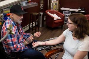 Tattoo artist Mario Singh explains tattoo care steps to first-time tattoo recepient Cassidy McGrann during Taku Tattoos International Suicide Survivors Day event on Saturday, Nov. 23, 2019. (Michael S. Lockett | Juneau Empire)