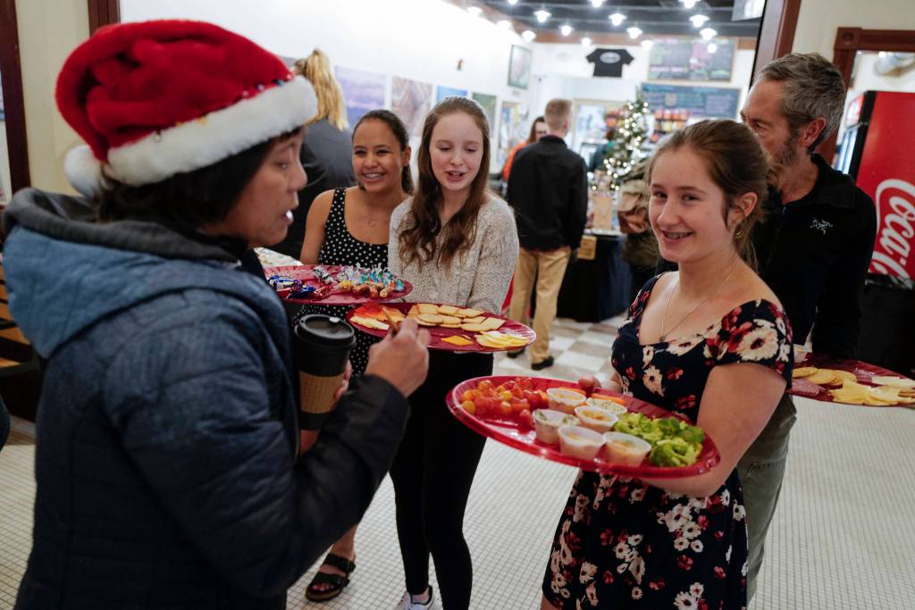 Adelie McMillian, right, Lydia Powers, center, and Dominique Morley, all members of figure skating team, serve trays of treats to visitors to the Senate Building during Gallery Walk on Friday, Dec. 6, 2019. (Michael Penn | Juneau Empire)