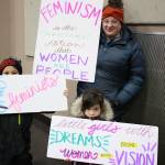 Ikahn Deguzman, 7, Courtney Deguzman and Hollis Deguzman, 4, stand with their signs after marching from the Alaska State Capitol to Centennial Hall, Saturday, Jan. 18, 2020. (Ben Hohenstatt | Juneau Empire)