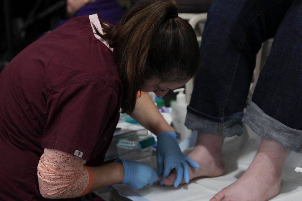 Lia Sickoria, a registered nurse at Bartlett Regional Hospital, cleans a guests feet at the Juneau Coalition for Housing and Homelessness 9th annual Homeless Connect event at the Juneau Arts and Culture Center Wednesday. (Michael S. Lockett | Juneau Empire)