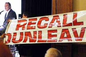 In this March 26 photo, protesters unfurl a banner as Gov. Mike Dunleavy speaks during a roadshow with Americans for Prosperity in 49th State Brewing Company in Anchorage. (Bill Roth | Anchorage Daily News via AP, File)