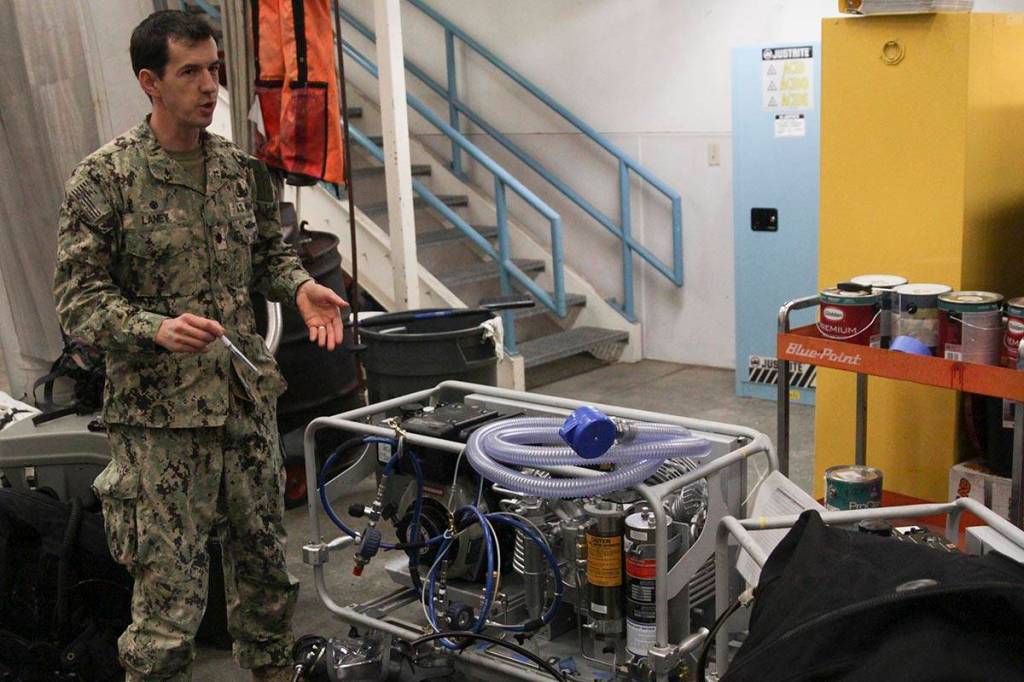 Navy Cmdr. John Laney, commanding officer of Mine Countermeasure Division 31, demonstrates the diver gear the unit uses at Coast Guard Station Juneau, Feb. 29, 2020. (Michael S. Lockett | Juneau Empire)