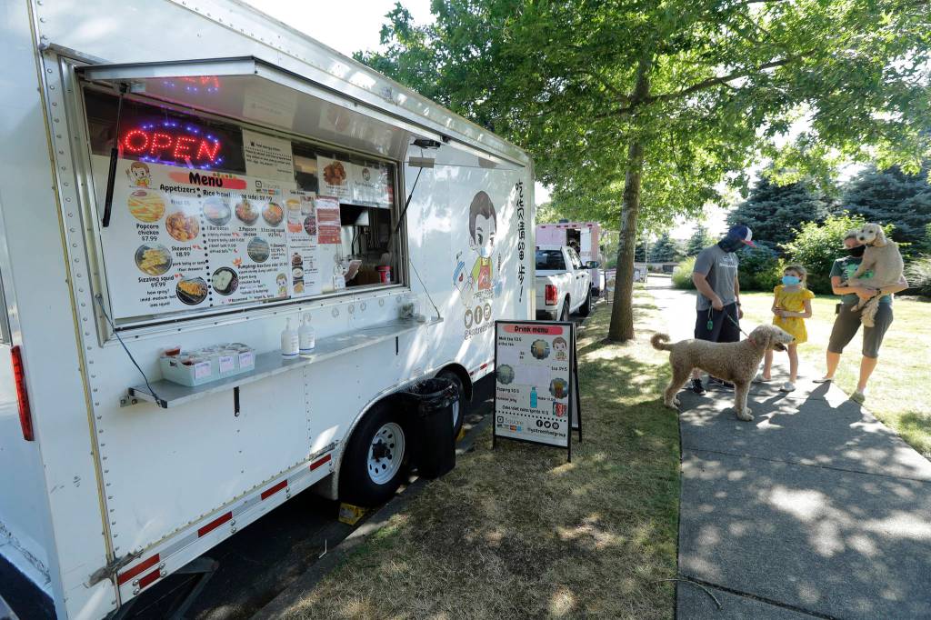 Bobby Price, left, and Catherine Vogt, right, stand with Catherines daughter Avery, 8, and their dogs as they wait to order from the YS Street Food food truck, Monday, Aug. 10, 2020, near the suburb of Lynnwood, Wash., north of Seattle. Long seen as a feature of city living, food trucks are now finding customers in the suburbs during the coronavirus pandemic as people are working and spending most of their time at home. (AP Photo / Ted S. Warren)