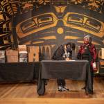 SHI President Rosita Worl and the late Cyril Georges daughter, Roberta Jack, sign a deed of gift at a transfer ceremony last week with the photo collection visible in the background. (Courtesy Photo / Lyndsey Brollini, Sealaska Heritage)