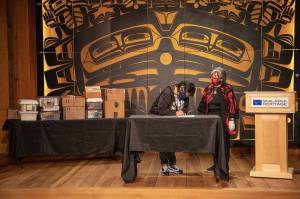 SHI President Rosita Worl and the late Cyril Georges daughter, Roberta Jack, sign a deed of gift at a transfer ceremony last week with the photo collection visible in the background. (Courtesy Photo / Lyndsey Brollini, Sealaska Heritage)