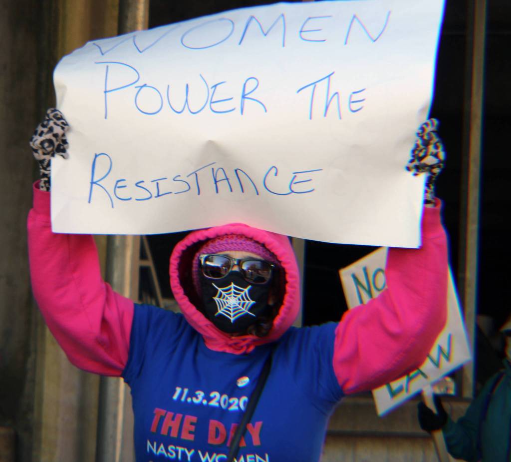 Gina Chalcroft holds up a sign stating Women power the resistance on Saturday, Oct. 17. (Ben Hohenstatt / Juneau Empire)