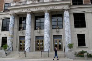 FILE - In this May 18, 2020 file photo, a woman walks past the Alaska Capitol in Juneau. Alaska lawmakers are set to convene amid a near decade-long run of deficits and economic fallout from the ongoing coronavirus pandemic. Go-to reserve accounts are depleted, and tough decisions await on how to use the state's nest-egg oil-wealth fund. It's unclear who will lead those debates: neither the House nor the Senate has organized. (AP Photo/Becky Bohrer, File)