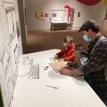 Sebastian Taylor-Manning pauses to sketch at a replica of an Alaskan illustrator’s desk. His brother McClain Taylor-Manning and his father, Chris Taylor, look on during a recent visit to the State Museum to see the new exhibit, "Illustrating Alaska: Artists Making Children’s Books", on display through April 3. (Courtesy Photo/Jackie Manning)