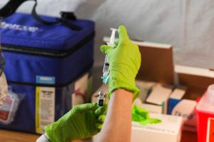 A health worker prepares a dosage of COVID-19 vaccine at a clinic at Centennial Hall on Feb. 11. A surge in vaccine availability means more people can get the vaccine, but so far few people are being required to get it. (Michael Lockett / Juneau Empire file)