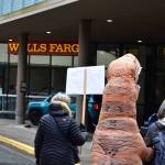 Environmental activists from 350Juneau, one dressed in a dinosaur costume, delivered a letter addressed to the CEO of Wells Fargo to the banks branch in downtown Juneau on Friday, April 2, 2021. The letter called on the bank to divest from fossil fuels. (Peter Segall / Juneau Empire)
