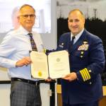 Capt. Stephen White, right, presents a commendation to City and Borough of Juneau Docks and Harbors port director Carl Uchytil during an Assembly meeting on May 24, 2021. (Dana Zigmund / Juneau Empire)