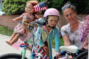 Imogen Resneck, 4, and Jamie Buehner finish up decorating a bike outside the Douglas Public Library parking garage on July 3, 2021. Resnecks doll, Robbie, was bound to the bike like an amber-haired figurehead because she wanted to go to the parade, Resneck said. (Ben Hohenstatt / Juneau Empire)
