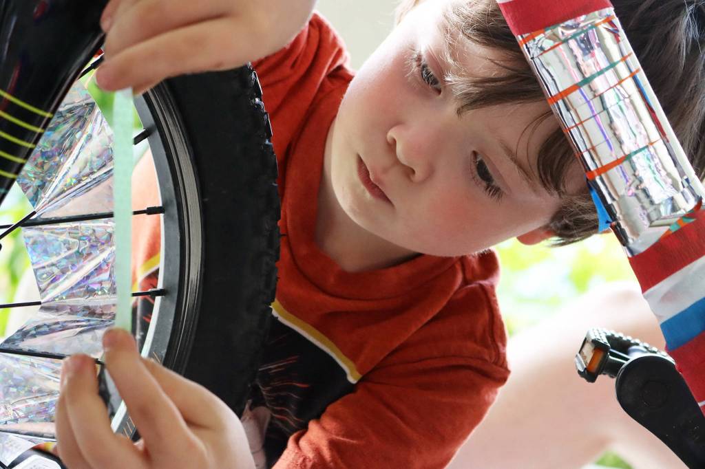 Kingston Wilson, 7, applies reflective decorations to a bike on July 3. Dozens of youths showed up to decorate their bikes -a day before Douglas held its parade. Wilson said he had not yet made up his mind whether he would ride in the parade, but said he liked the stars decorating his bike. (Ben Hohenstatt / Juneau Empire)