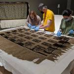 Courtesy Photo / Chelsea Kilgore, Alaska State Library Archives and Museum 
From left to right: Jackie Manning, curator of exhibits for the Alaska State Library, Archives and Museum; Aaron Elmore, exhibit designer, and Ellen Carrlee, conservator for the museum unpack an ancient ravens tail robe on loan from the Royal Ontario Museum in Canada. This robe is one of only about a dozen older robes in existence, according to SLAM collections curator Steven Kenrikson, and will only be on display at SLAM until next month.