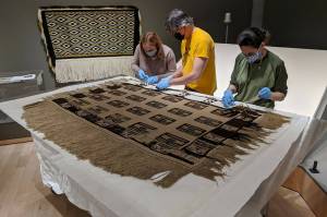 From left to right: Jackie Manning, curator of exhibits for the Alaska State Library, Archives and Museum; Aaron Elmore, exhibit designer, and Ellen Carrlee, conservator for the museum unpack an ancient raven's tail robe on loan from the Royal Ontario Museum in Canada. This robe is one of only about a dozen older robes in existence, according to SLAM collections curator Steven Kenrikson, and will only be on display at SLAM until next month. (Courtesy Photo/ Chelsea Kilgore, Alaska State Library Archives and Museum)