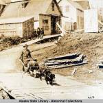 This photo from the Capt. George H. Whitney Photograph Collection shows a man, with wheelbarrow cart and two dogs in harness, transports beer barrels along boardwalk; pedestrians, buildings, and sign for Coons Drugstore in background in Juneau in 1886. Juneau and Douglas breweries were the subject of the Gastineau Channel Historical Societys award-winning newsletter. (William Howard Case/ Alaska State Library - Historical Collections)