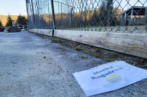 A sign reading Masks Required lies on the ground near a softball field at Melvin Park in this May photo. The City and Borough of Juneau is lowering the community risk level for COVID-19, but masks remain required inside public spaces. (Ben Hohenstatt / Juneau Empire)