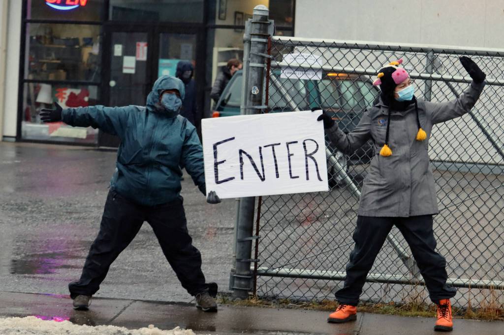 Abbey Greer and Kelsey Rich show drivers the way in to the Salvation Armys meal distribution site on Thursday. (Ben Hohenstatt / Juneau Empire)