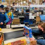 Alaska State Trooper Patrol Sergeant Chris Russell, Weldon and Keane look on as Fred Meyer employee Judy Magalotti checks them out during the annual Shop with a Cop event on Dec. 18, 2021. (Michael S. Lockett / Juneau Empire)