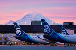 Alaska Airlines planes are parked at gates with Mount Rainier in the background at sunrise, March 1, 2021, at Seattle-Tacoma International Airport in Seattle. Alaska Airlines said Thursday, Jan. 6, 2022, it will trim its schedule by about 10% for the rest of January at it deals with unprecedented numbers of employees calling in sick during the current COVID-19 surge. (AP Photo / Ted S. Warren, File)