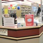 A collection of signs advising patrons about various COVID-related issues sits atop the front desk at the Douglas Branch of the Juneau Public Library on Jan. 6. (Dana Zigmund/Juneau Empire)