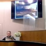 Officer John Waldron of the Yakutat Borough Police Department looks at a print of a photograph as he testifies about a stabbing he responded to in 2018. (Screenshot)